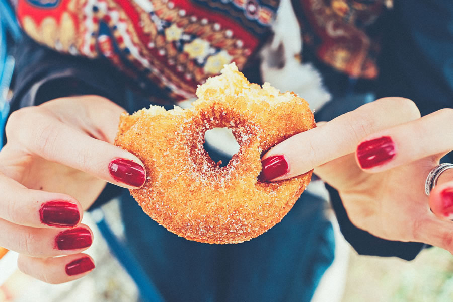 a woman hands holding a sugary donut with red nails