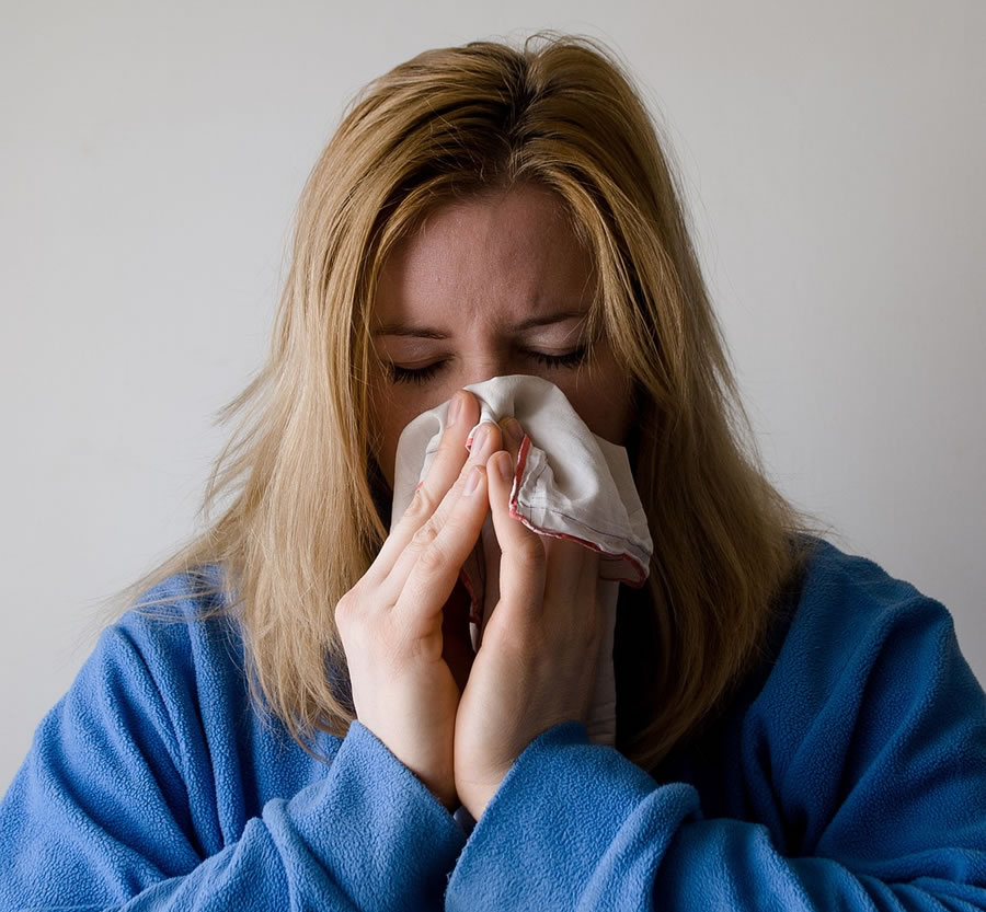 A woman with blonde hair in a blue robe blowing her nose