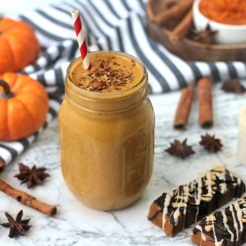 pumpkin pie protein shake in a mason jar next to pumpkin protein bar on marble next to mini pumpkins