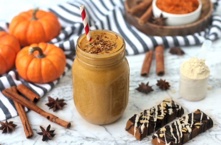 pumpkin pie protein shake in a mason jar next to pumpkin protein bar on marble next to mini pumpkins