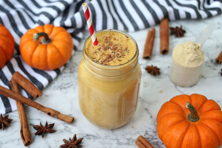 pumpkin pie protein shake in a mason jar next to pumpkin marble next to mini pumpkins and cinnamon sticks